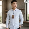 Người mẫu nam với kiểu tóc undercut nam tính đang diện áo sơ mi dài tay màu trắng của Burberry phối cùng quần tây đen, tay áo bên trái xắn nhẹ lộ viền kẻ sọc, ngực áo đính tag giấy nâu sang trọng.